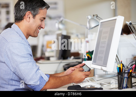 Man Using Mobile Phone At Desk In Busy Creative Office Stock Photo