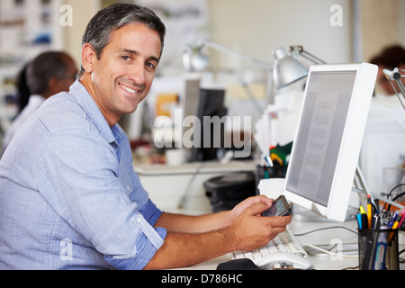 Man Using Mobile Phone At Desk In Busy Creative Office Stock Photo