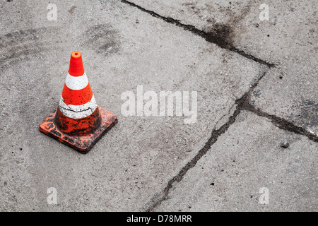 Red and white striped warning cone on dirty asphalt road Stock Photo