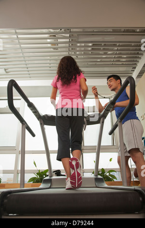 Woman walking on treadmill, trainer standing with stopwatch Stock Photo