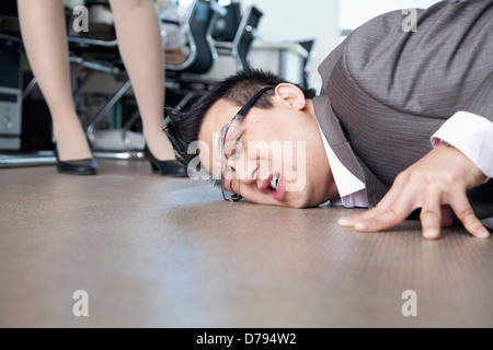 Businessman with face on the floor, coworker standing by him Stock Photo