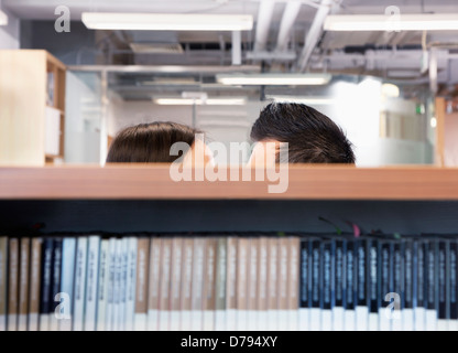 Work romance between two business people hiding behind shelves Stock Photo