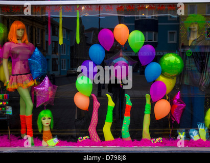Bright lurid colourful gaudy fluorescent party clothes on display in a fancy dress shop window, UK Stock Photo