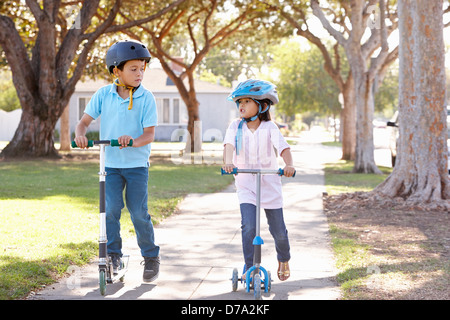 Boy And Girl Wearing Safety Helmets And Riding Scooters Stock Photo