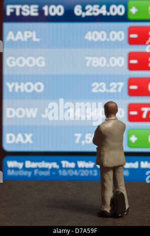 Close up of Toy small business man businessman figure looking at FTSE 100 Index screen finance business concept Stock Photo