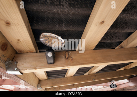 Small LED night light with PIR fitted underneath a leanto bitumen roof with wired operating solar panel Stock Photo
