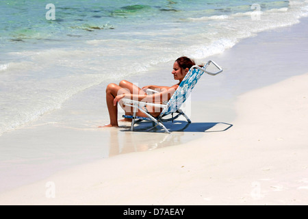 A young woman sits in her collapsible chair letting her feet be washed over by the surf on Siesta Key beach FL Stock Photo