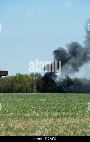 Black smoke rises into a blue sky from a fire on an old airfield in Essex as a pile of tyres burn. Stock Photo