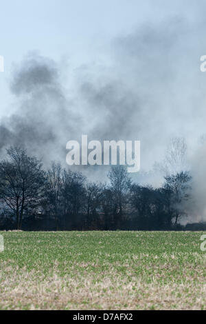 Black smoke rises into a blue sky from a fire on an old airfield in Essex as a pile of tyres burn. Stock Photo