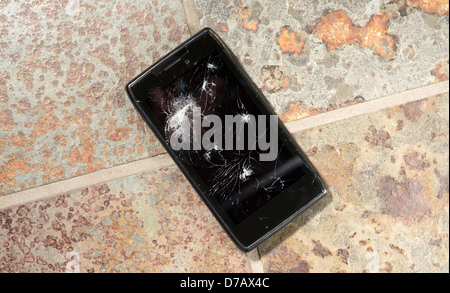 Dropped smartphone on hard floor with cracked screen. Stock Photo