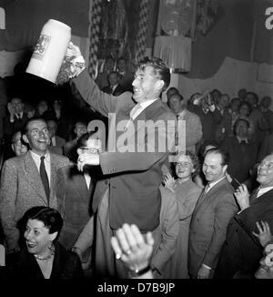 Enthusiastic welcome of the German national football team in Munich's Loewenbraeukeller brewery on the 6th of July in 1954, where team captain Fritz Walter is holding up a beer mug and is announced honorary team captain of the German team. At the bottom left his wife Italia. Stock Photo