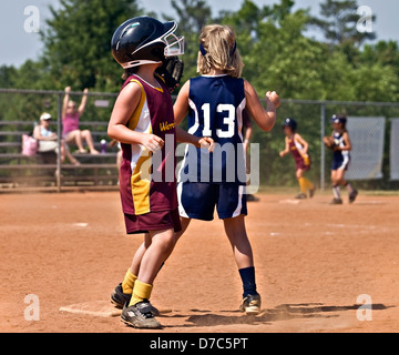 Young girls during a softball game making runs after a hit. Stock Photo