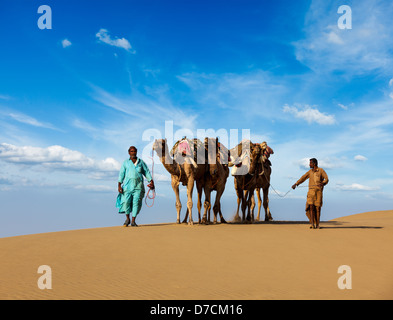 Rajasthan travel background - Indian cameleers (camel drivers) with camels in dunes of Thar desert. Jaisalmer, Rajasthan, India Stock Photo