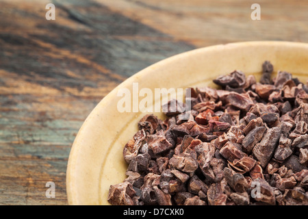 Raw cacao nibs in a small ceramic bowl against grunge wooden background Stock Photo