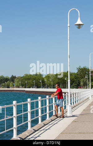 A man stands looking out over the railing at the beautiful blue harbor on the boardwalk in Sarnia Ontario, Canada Stock Photo