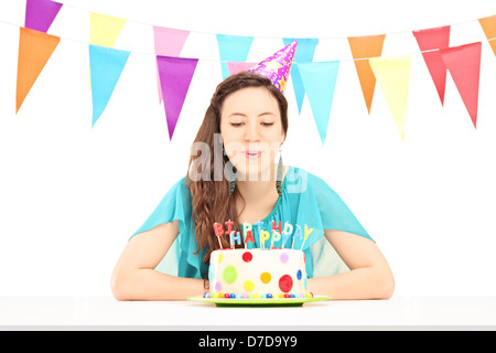 A smiling birthday female with a party hat blowing the candles on her birthday cake isolated against white background Stock Photo