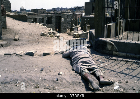 A homeless person sleeping in the ground amid dense grid of tomb and Islamic mausoleum structures in the City of the Dead or Cairo Necropolis where some people live in southeastern Cairo, Egypt. Stock Photo