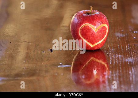 Red wet apple with heart shape on wooden desk Stock Photo