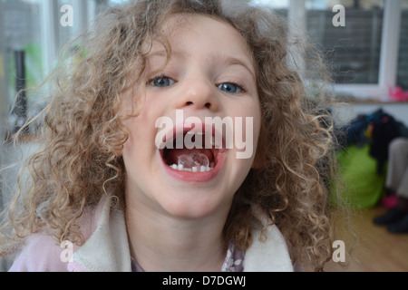 Five year old girl with curly hair and blue eyes showing an ice cube in her open mouth Stock Photo
