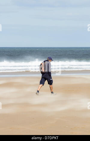 Man walking through wind blown sand on a breezy Bank holiday Saturday on Redcar beach, Redcar, Cleveland, north east England, UK. Stock Photo