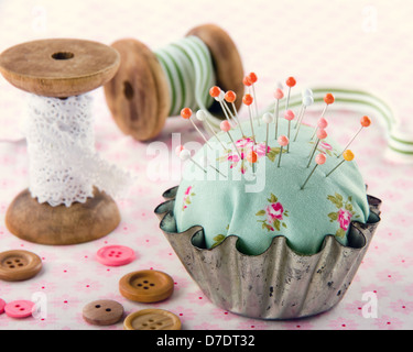 Green handmade floral pincushion in an old metal cupcake with buttons and spools of thread and lace, sewing concept background Stock Photo
