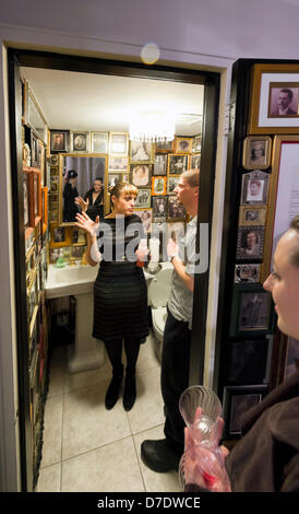 Huntington, New York, USA. 4th May, 2013. Artist LAUREN WEISSLER, left, in the bathroom of fotofoto Gallery, is showing visitors the art installation called The American Family Gallery Project, by artist Jeffrey R. Smith, shown here during an Opening Reception at the cooperative photography gallery which is a non-profit organization. Many of the photographs used for the installation are of relatives of Smith and photo photo artists. Stock Photo