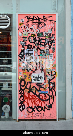 Graffiti, stickers and tags on the door to Grippo art + design clothing store on Grand Street in Williamsburg, Brooklyn, New York