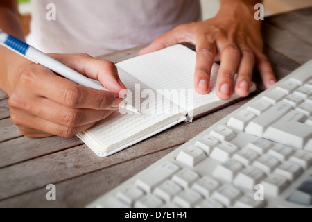 Photo of hands writes a pen in a notebook, computer keyboard on foreground Stock Photo