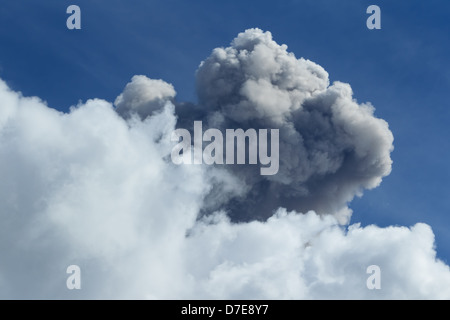 A large, dense cumulus cloud formation dominates the frame, with a mix of bright white and dark gray tones indicating depth and shadow. The cloud rises vertically against a clear, deep blue sky with Stock Photo