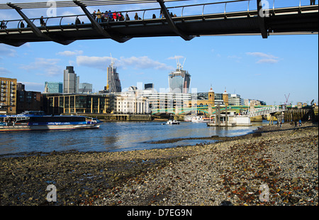 View of the City of London from the shore of the Thames,underneath the Millennium bridge at low tide Stock Photo