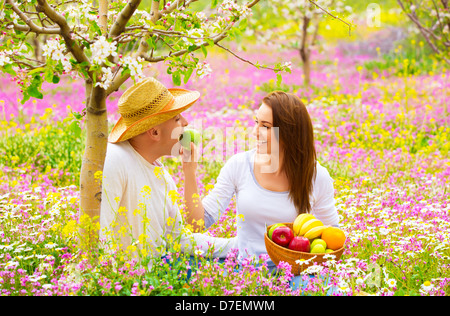 Young happy family having fun in spring blooming garden, cute woman feeding her boyfriend apple, romance and love concept Stock Photo