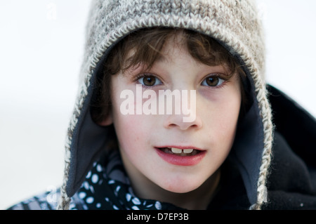 close up of an eight year old boy wearing a woolly winter hat outdoors in the snow Stock Photo