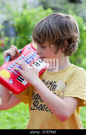 Portrait of a boy with keyboard playing outdoor in the garden. Stock Photo