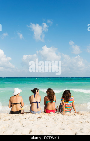 four young women in conversation on a beach  sitting and facing the sea Stock Photo