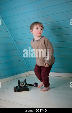 A boy is about to run from a telephone to fetch someone. The old fashioned phone standing on the floor with receiver of the hook Stock Photo