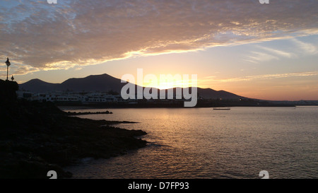 Sun rising over mountains by the sea with reflection on clouds and water Stock Photo