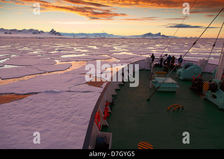 Icebreaker Ortelius moving through ice at sunset / sunrise as we travel below the Antarctic Circle, Antarctica.  Stock Photo