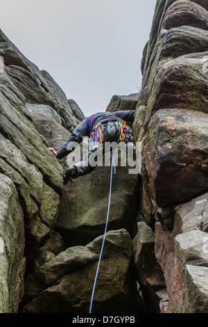 Grey sky clearing over a male climber on Flying Buttress Gully - Diff at Stanage Edge Stock Photo