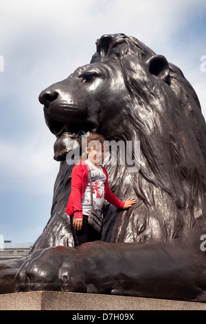 A child having her photo taken climbing on a lion statue, Trafalgar Square, Central London UK Stock Photo