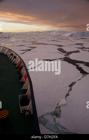 Icebreaker Ortelius moving through ice at sunset / sunrise as we travel below the Antarctic Circle, Antarctica.  Stock Photo