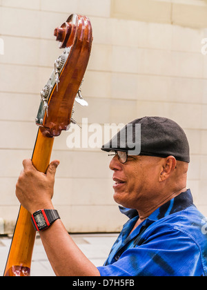 A male Cuban street musician plays his bass and sings as he looks to the side with his mouth open in Havana, Cuba. Stock Photo
