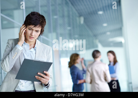 Image of busy female calling on the phone and reading document in working environment Stock Photo