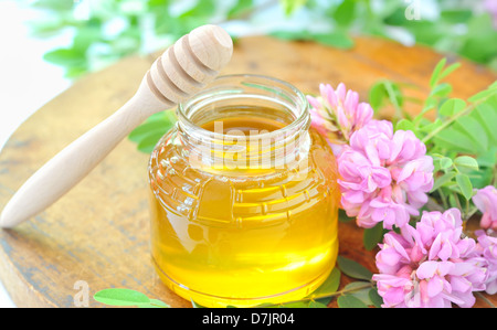 jar full of honey and stick with acacia pink and white flowers Stock Photo