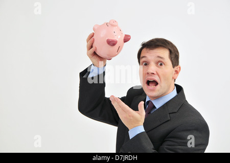 Businessman with a worried expression on his face, holding a piggy bank upside down. Stock Photo