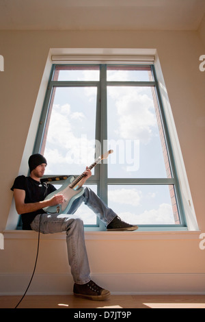 Low angle view of young man sitting on window sill and playing electric guitar Stock Photo