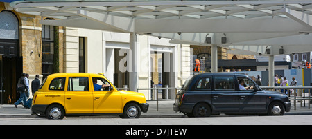 Black cab with no advertising next to a yellow taxi with advert at a London station pickup rank Stock Photo