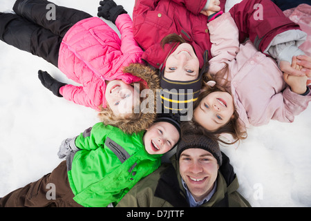 Directly above portrait of three children (2-3, 4-5) with parents lying on snow Stock Photo