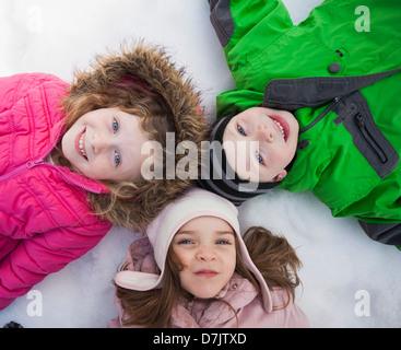 Directly above portrait of three children (2-3, 4-5) lying on snow Stock Photo