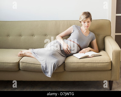 Pregnant woman lying on sofa reading Stock Photo