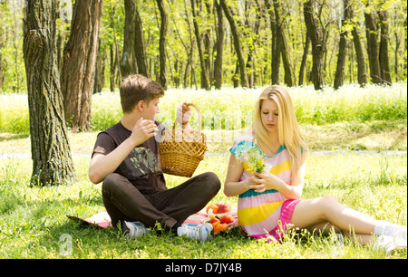 Photograph of a couple on a sweet picnic date, boy picking something from the basket while girl playing with a flower.